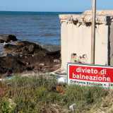 Inghiottito dall�erba e dalle bottiglie di plastica si trova poi un cartello che segnala il divieto di balneazione